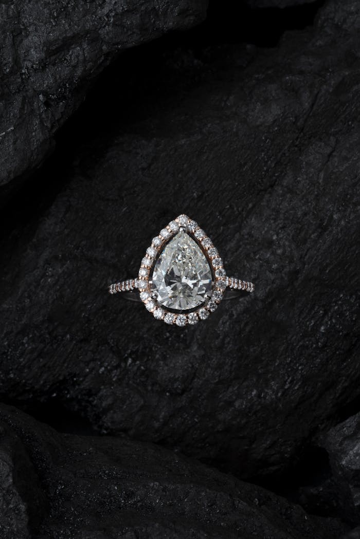 why-choose-us Stunning teardrop diamond ring surrounded by smaller stones on a textured dark background.