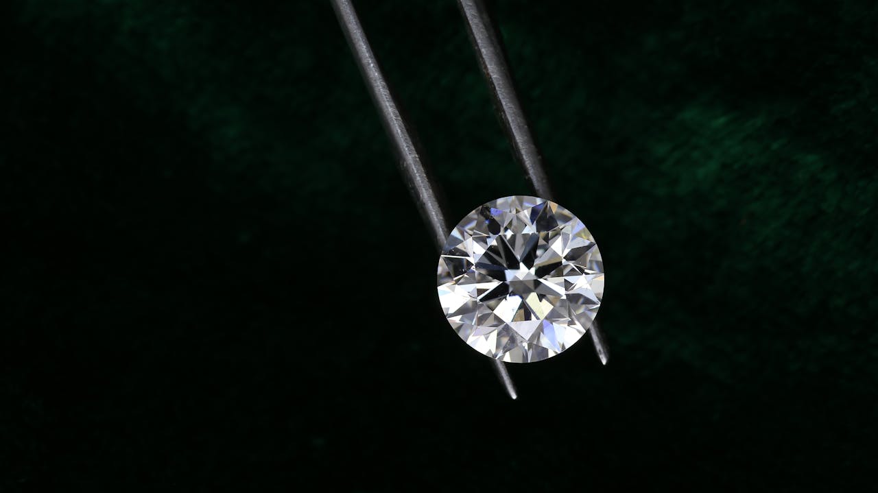 home-hero A sparkling round diamond is delicately held by tweezers against a dark textured background.